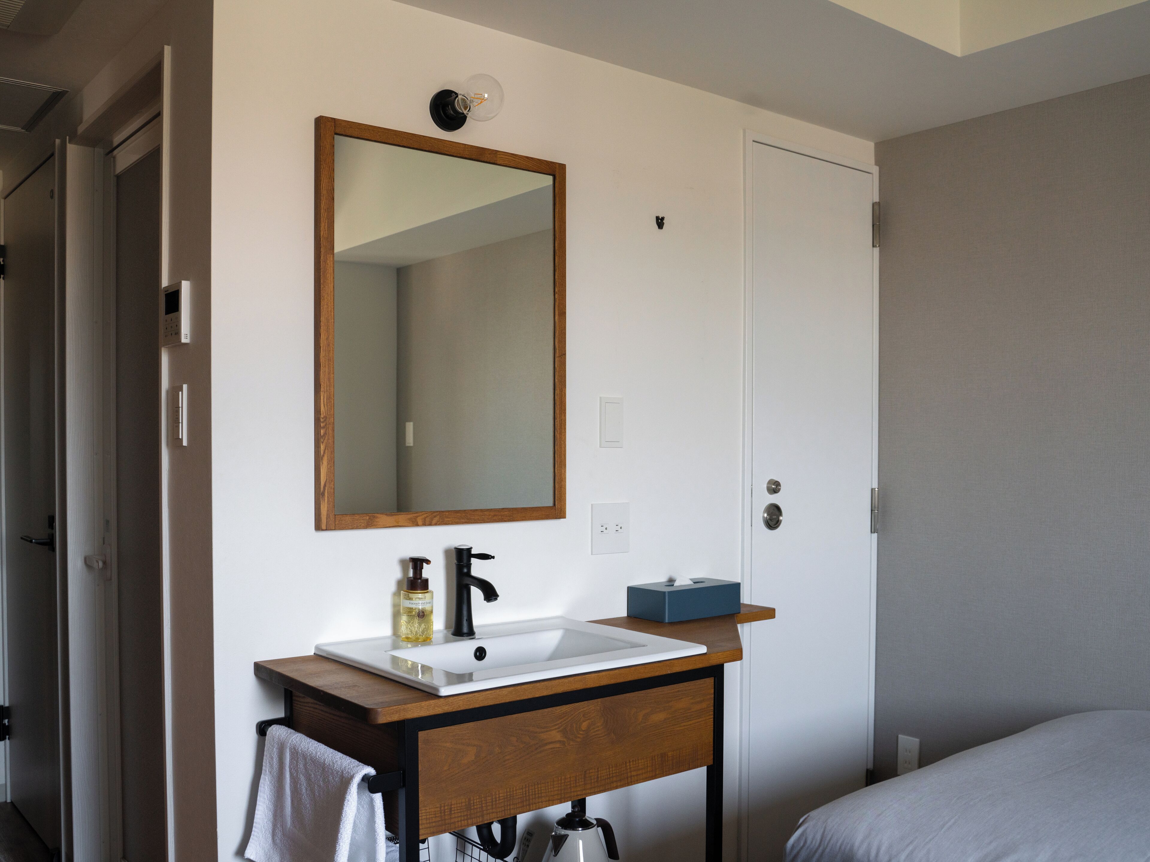 A bathroom with a wooden vanity, a mirror, a sink, a towel, and a door.