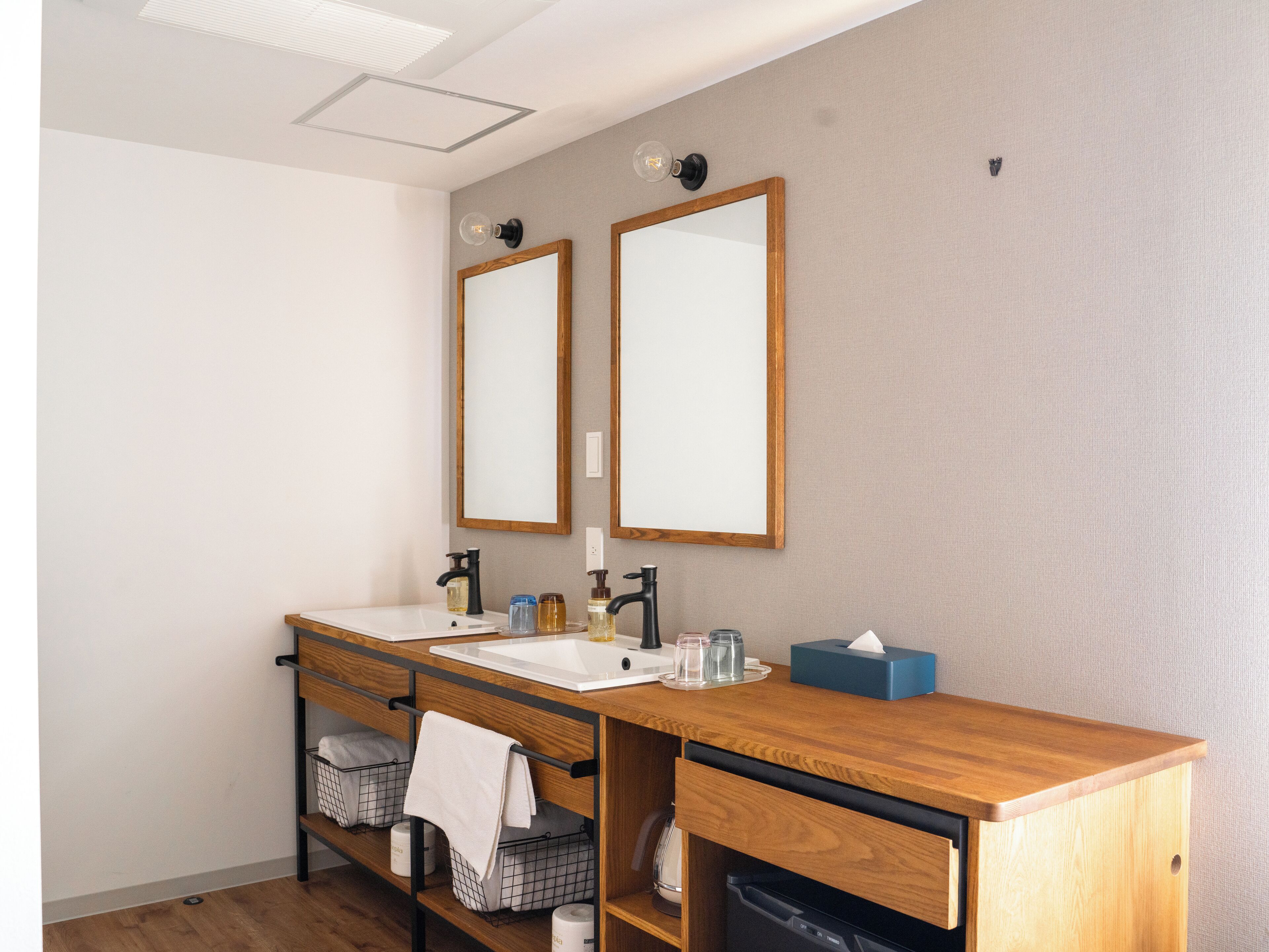 A modern bathroom with two mirrors, a wooden vanity, a sink, and a towel rack.