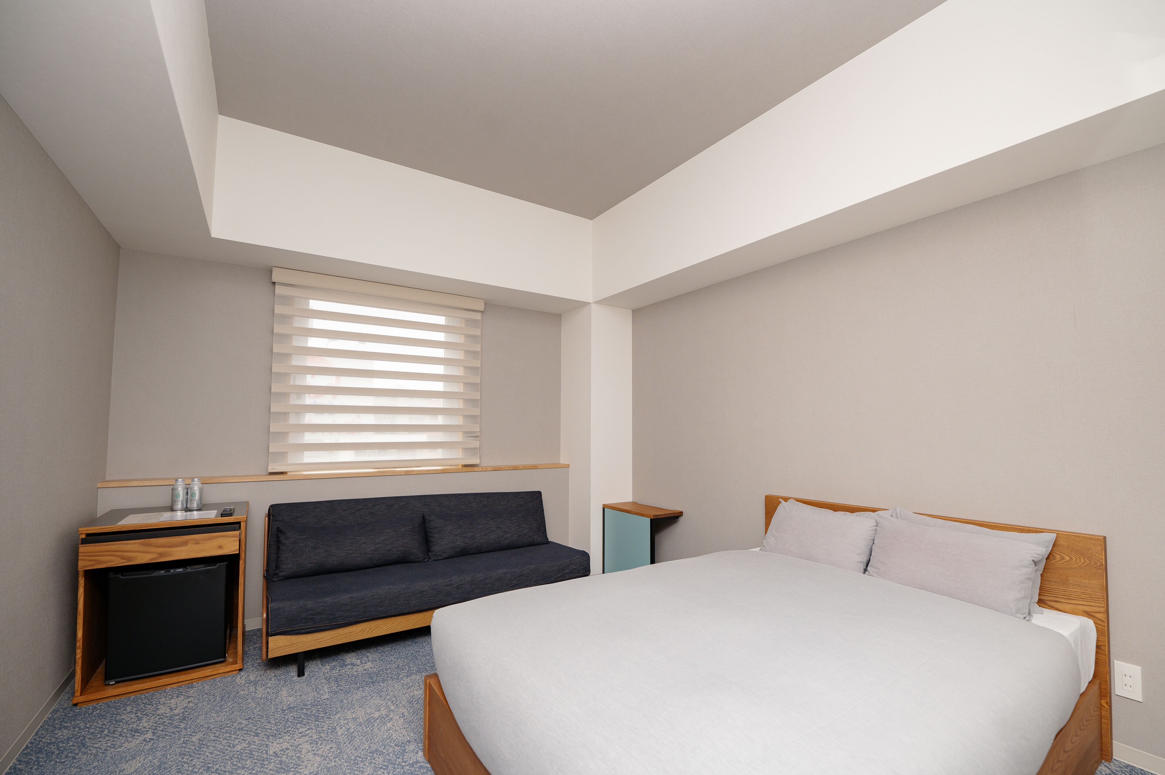 A bedroom with a bed, a sofa, a small desk, and a window with blinds.