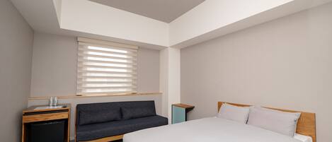 A bedroom with a bed, a sofa, a small desk, and a window with blinds.