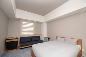 Une chambre à coucher avec un lit, un canapé, un petit bureau et une fenêtre avec des stores.