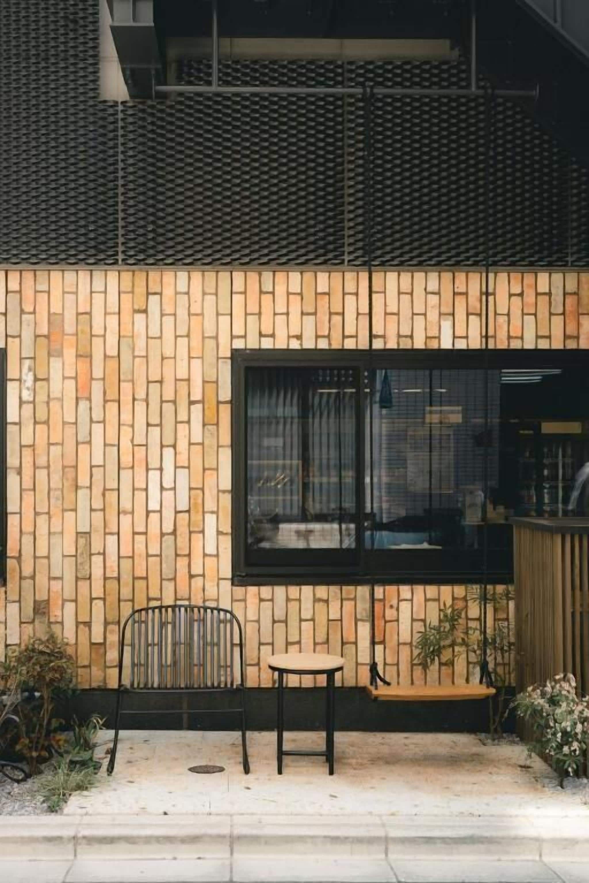 A brick-patterned exterior wall with a window, a small table, a chair, and a swing.