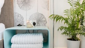 A modern room with a light blue bench, a floor lamp, a potted plant, and a wall with a dandelion pattern. - Tropical Garden Oasis (Birmingham)