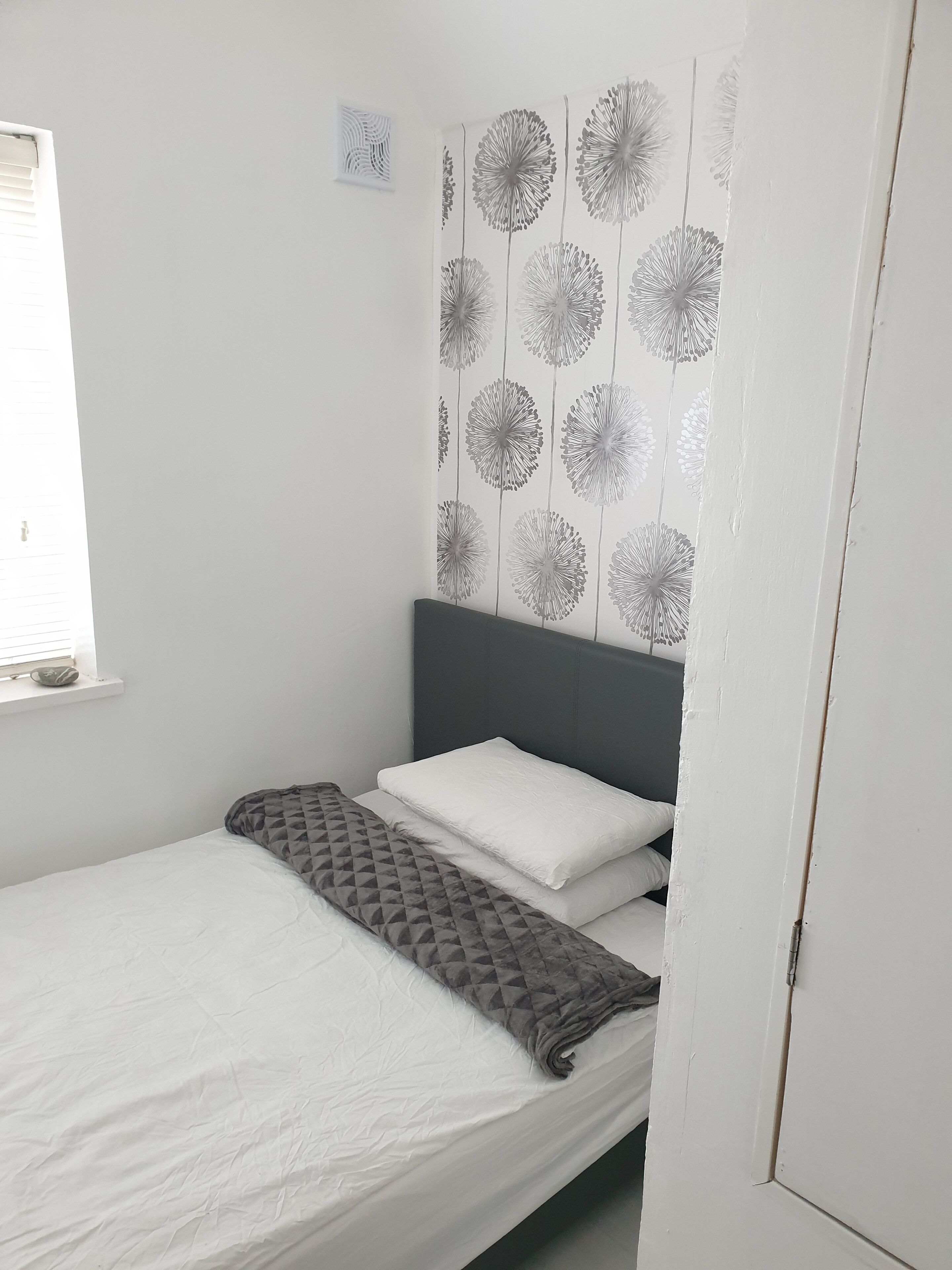 A small, neatly made bed with a grey headboard and white bedding.