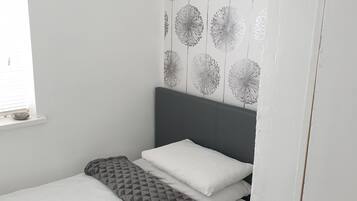 A small, neatly made bed with a grey headboard and white bedding.