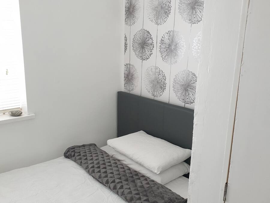 A small, neatly made bed with a grey headboard and white bedding.