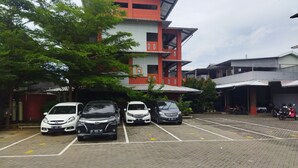 A parking lot with several cars and a building with a red and white facade. - Hotel O Kost Orange Syariah (Makassar)