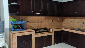 A kitchen with dark wooden cabinets, a tiled backsplash, a sink, and a stove. - Hotel O Kost Orange Syariah (Makassar)