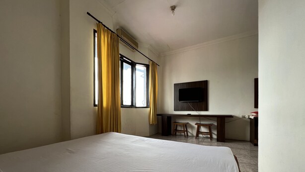 A hotel room with a large bed, a desk with two chairs, a flat-screen TV mounted on the wall, and a window with curtains. - Hotel O Kost Orange Syariah (Makassar)
