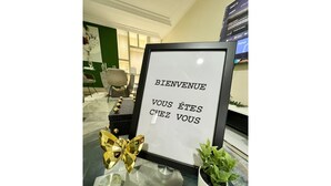 Une pancarte d’accueil encadrée, ornée d’un nœud doré, et une plante en pot placée à côté.