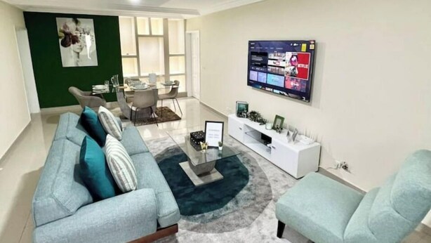 Un salon moderne avec un canapé, un fauteuil et un téléviseur fixé au mur.