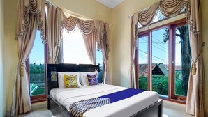 Una habitación de hotel con una cama grande, dos almohadas, una colcha de diseño azul y amarillo y cortinas.