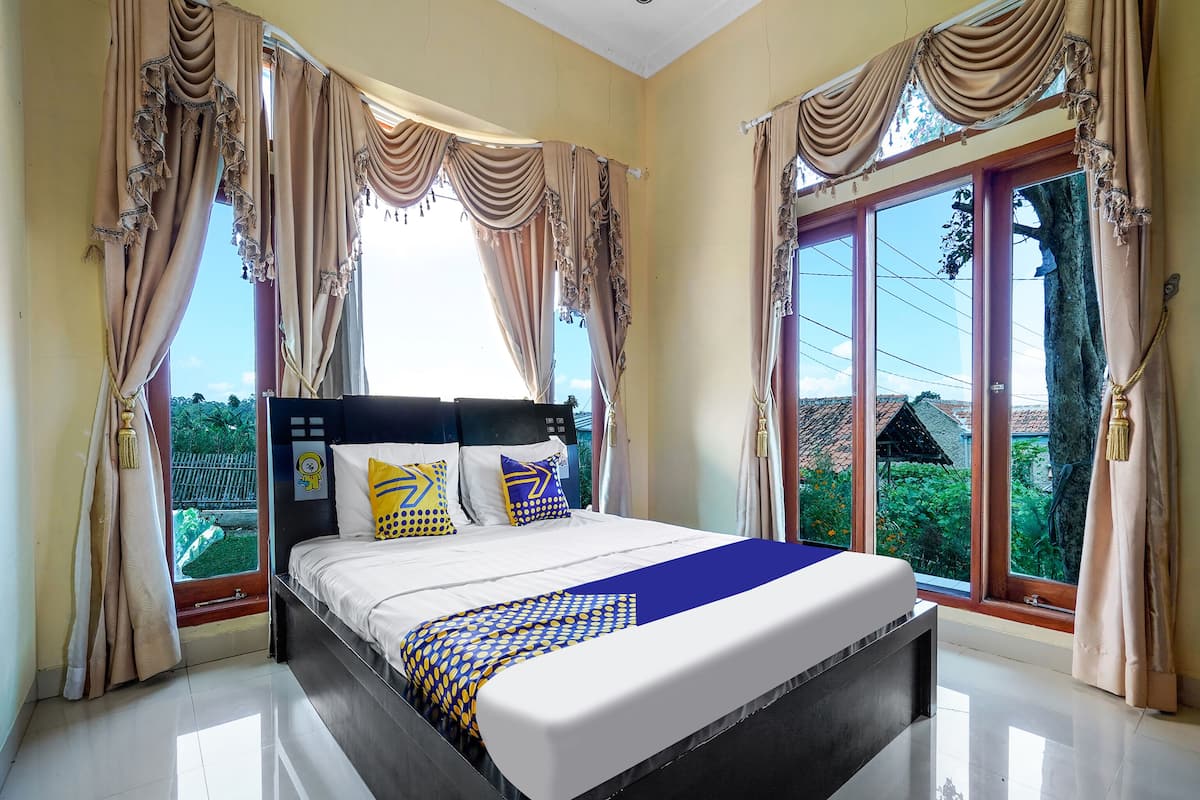 A hotel room with a large bed, two pillows, a blue and yellow patterned bedspread, and curtains.
