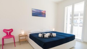 Hotellihuone, jossa on sänky, yöpöytä, tuoli ja ikkuna, josta on näkymä rakennuksiin.