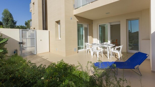 Un appartement moderne doté d’un balcon, d’un coin repas avec des meubles blancs et d’un fauteuil bleu.
