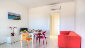 Un salon moderne comprenant un coin repas, un canapé rouge vif et un tableau représentant un paysage côtier.
