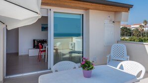 A balcony with a table and chairs, a potted plant, and a sliding glass door leading to an indoor area with a TV and seating. - Splendid attic with large veranda. (RAGUSA)