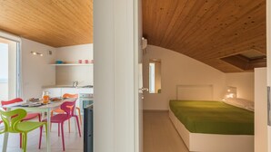 A compact room with a bed, a small kitchenette, and a dining area with colorful chairs. - Splendid attic with large veranda. (RAGUSA)