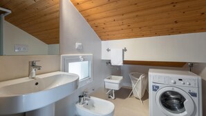 A modern bathroom with a wooden ceiling, a large sink, a bidet, a toilet, and a washing machine. - Splendid attic with large veranda. (RAGUSA)