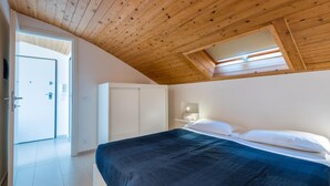 Une chambre avec un plafond en pente, un lit avec du linge de lit blanc, une table de chevet et une armoire.