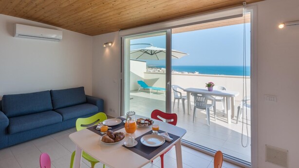 Une chambre moderne avec un plafond en bois, un canapé, une table à manger avec des chaises et un balcon offrant une vue sur la mer.