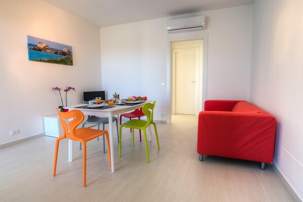 Una sala de estar moderna con comedor, que incluye un sofá rojo, sillas coloridas y un cuadro en la pared.