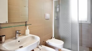 A bathroom with a white sink, a mirror, a glass shelf, a toilet, and a glass shower enclosure. - Modern and elegant apartment (RAGUSA)
