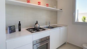 A modern kitchen with white cabinets, a gas stove, a kettle, and a stainless steel sink. - Modern and elegant apartment (RAGUSA)