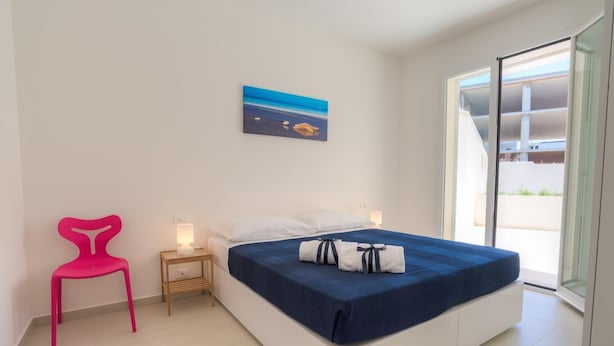 A modern bedroom with a bed, a nightstand, a chair, and a painting on the wall. - Modern and elegant apartment (RAGUSA)
