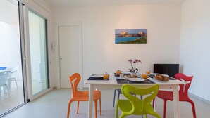 Un comedor con una mesa dispuesta para el desayuno, sillas coloridas y un cuadro con un paisaje en la pared.