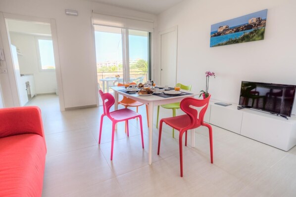 A bright living room with a dining area, a TV, and a painting of a coastal scene.