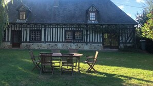 Un edificio de estilo Tudor tradicional con fachada de piedra y entramado de madera, que cuenta con un amplio césped y zona de estar al aire libre.