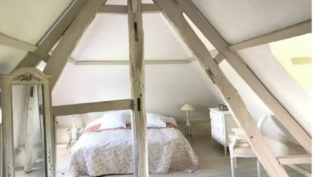 Un dormitorio con techo inclinado, una cama con colcha estampada, un aparador y una silla.