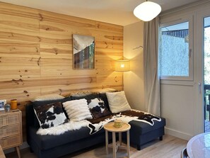 Una habitación acogedora con un panel de madera, un sofá cubierto con un plaid de cuero de vaca, una mesita redonda y una lámpara.