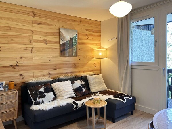 A cozy room with a wooden wall panel, a sofa with a cowhide throw, a small round table, and a lamp.