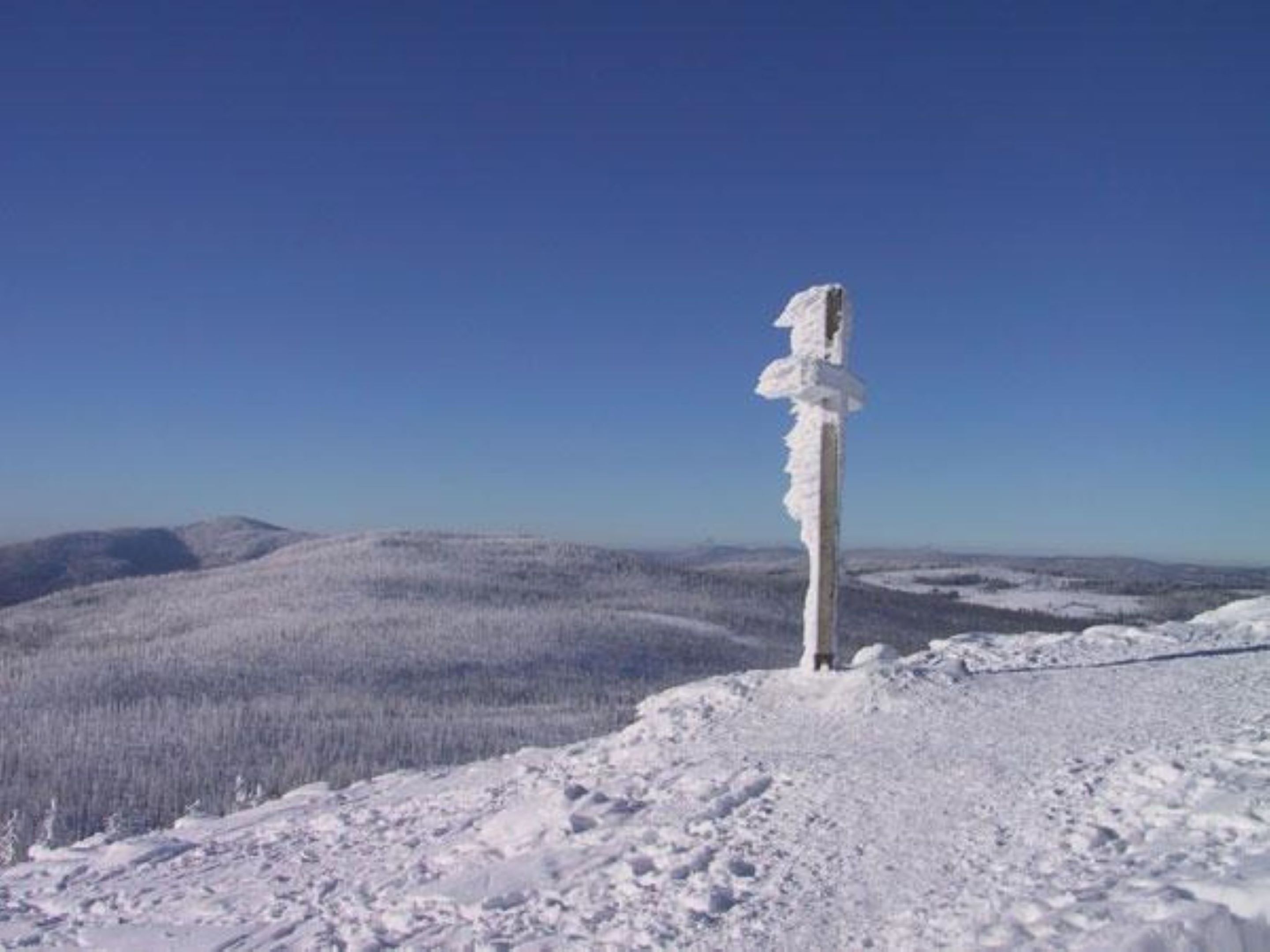 A snow-covered landscape with a tall, thin ice formation in the foreground.
