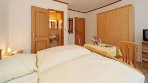 A bedroom with two beds, a wooden wardrobe, a small table with a vase of flowers, and a television on a wooden stand. - Pension Wiesengrund (Neuschoenau)