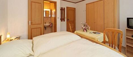 Un dormitorio con dos camas, un armario de madera, una mesita con un florero y un televisor sobre un mueble de madera.