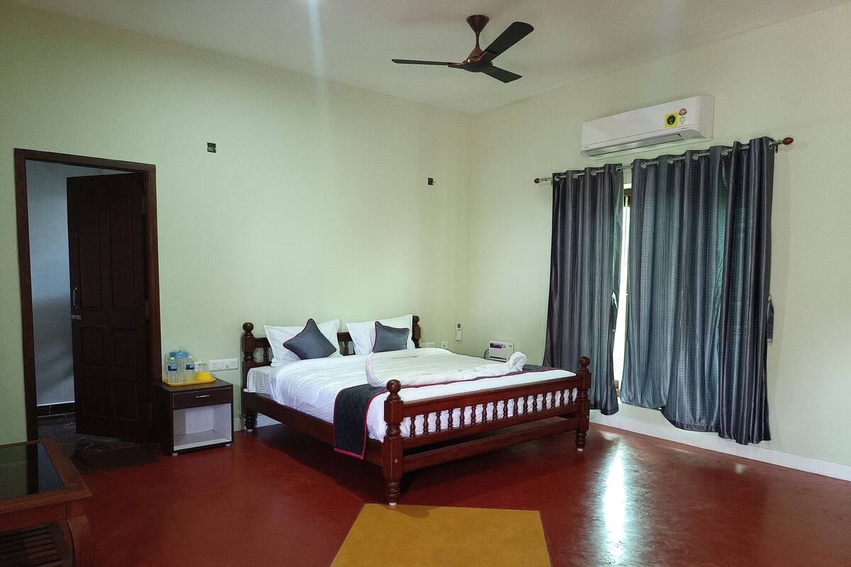 Une chambre à coucher comprenant un lit, une table de chevet, un miroir, un ventilateur de plafond et une fenêtre avec des rideaux.