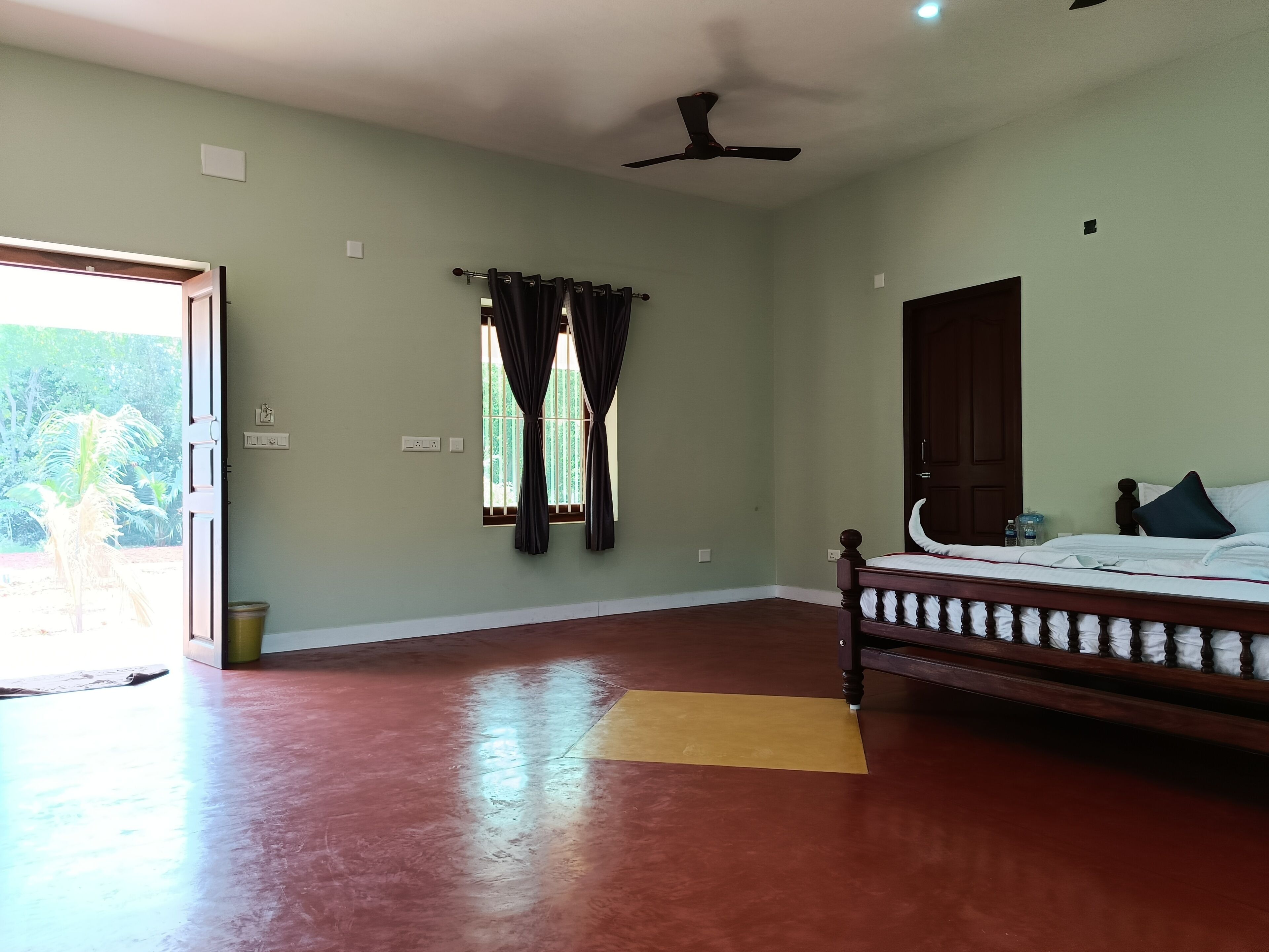 A bedroom with a bed, a ceiling fan, a window with curtains, and a door.