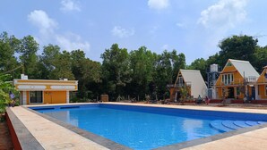 A swimming pool with a tiled edge, surrounded by buildings with a yellow facade and a blue roof. - Auro Sunrise Resort (Vanur)