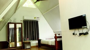 A bedroom with a sloped ceiling, a bed, a TV mounted on the wall, and a window with curtains. - Auro Sunrise Resort (Vanur)
