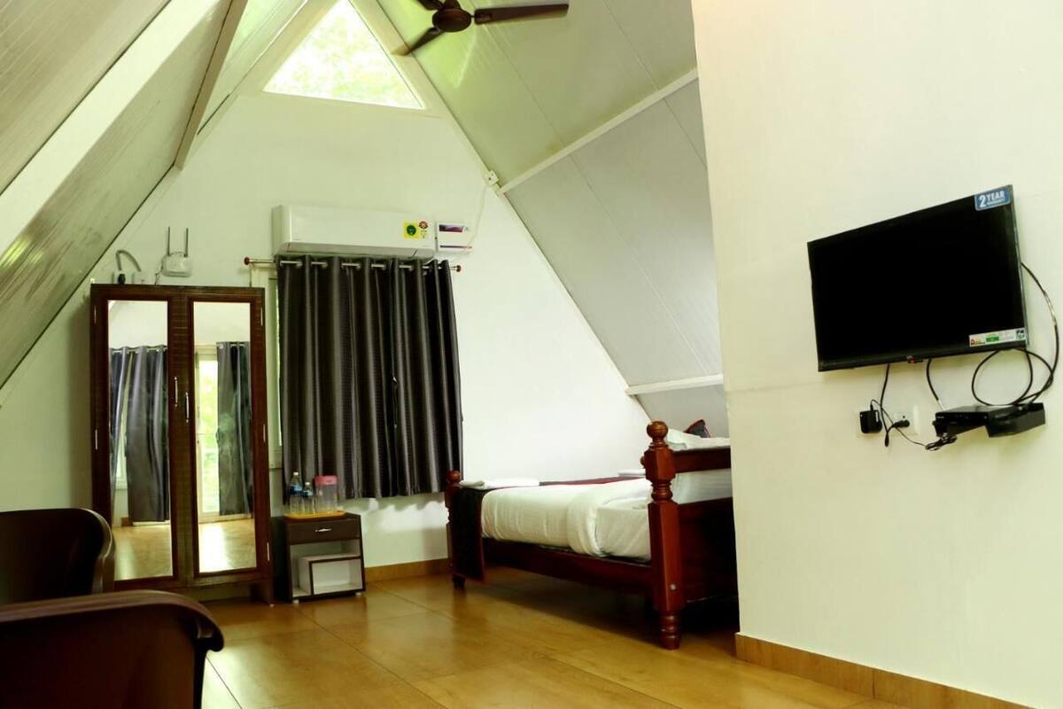 Une chambre avec un plafond en pente, un lit, un téléviseur fixé au mur et une fenêtre avec des rideaux.