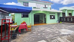 A two-story building with a green facade and a tiled roof. There is a covered outdoor area with a table and chairs, and a blue canopy. - Hotel O Desa Wisata NangelasariNearPasir Tulang (Nangelasari)