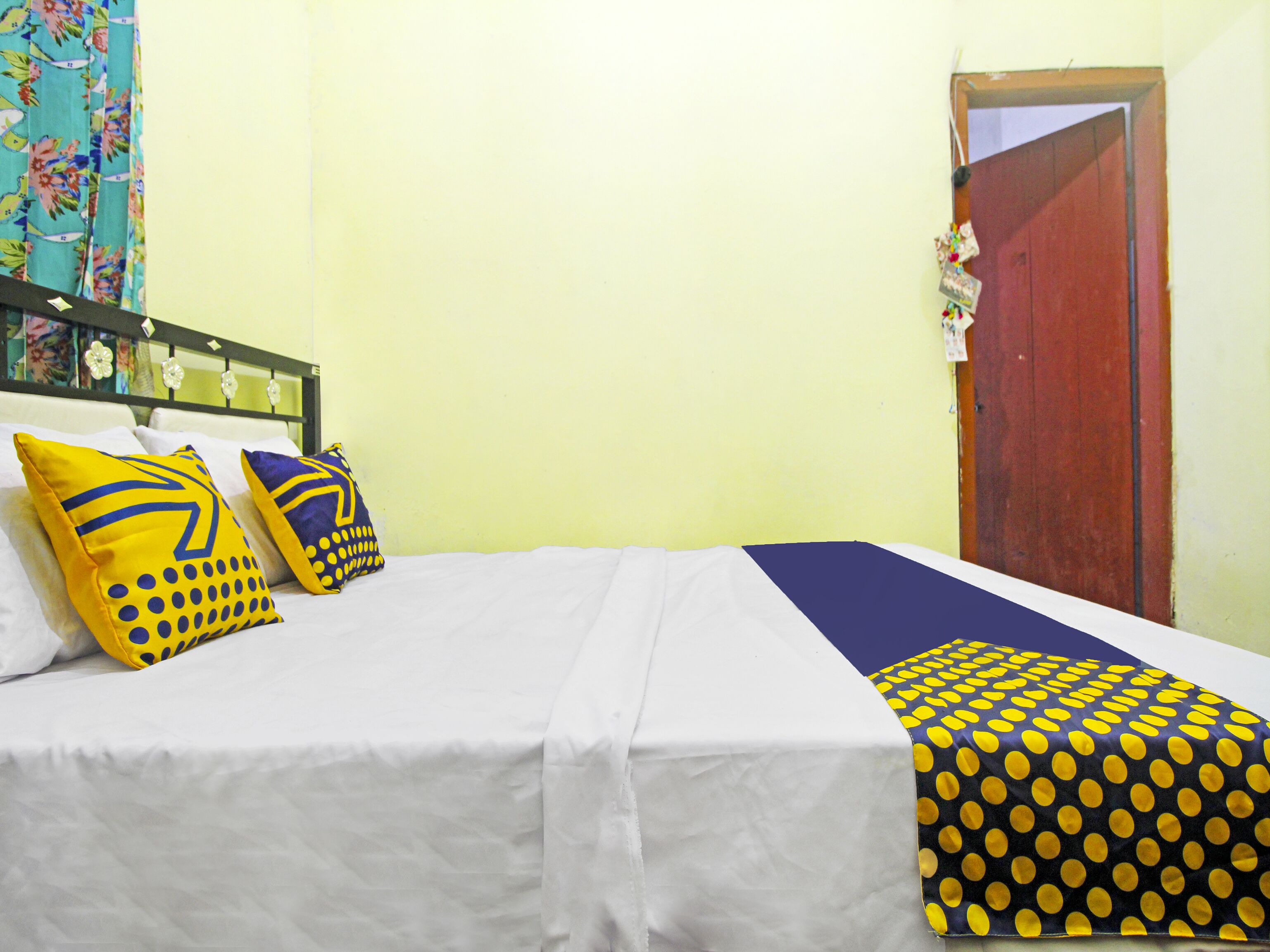 Una cama con ropa de cama blanca, dos almohadas con diseños amarillos y azules, y una manta de lunares azules y amarillos.