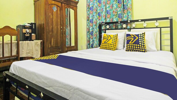 A bedroom with a bed, a wooden wardrobe, a desk with a computer, and a window with floral curtains. - Hotel O Desa Wisata NangelasariNearPasir Tulang (Nangelasari)