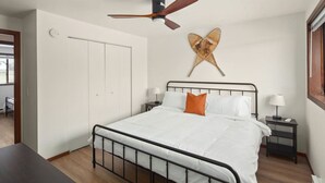 Ein Schlafzimmer mit einem Bett, einem Deckenventilator, einer Wanddekoration und einem Nachttisch mit Lampe.