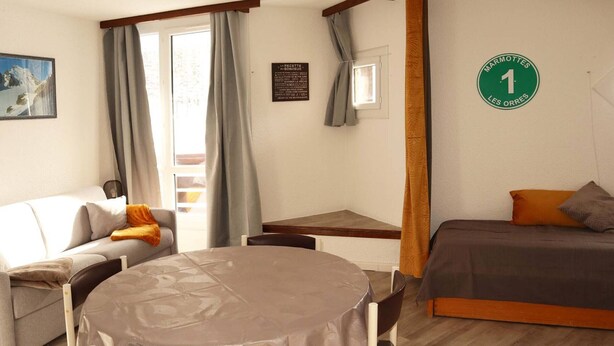 A cozy room with a round table, a sofa, a bed, and a window with curtains.