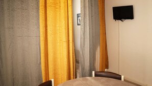A room with a round table, two chairs, a television mounted on the wall, and curtains in yellow and grey.