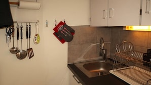 A kitchen with a stainless steel sink, a dish drying rack, and various utensils hanging on the wall.